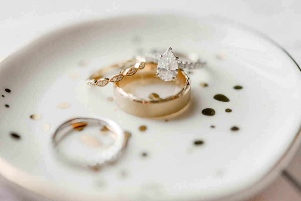 Bride and Groom's diamond engagement ring and wedding bands on a small ceramic plate