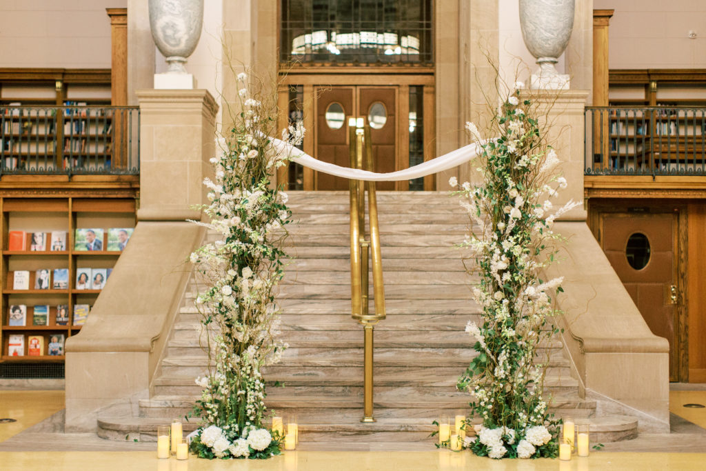 The wedding arch with white flowers, greenery and candles inside the Indianapolis central library