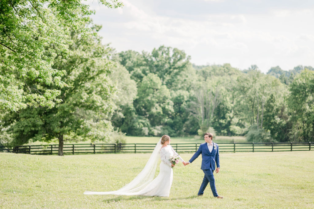 The bride and groom walk through a grass field on at their private property wedding