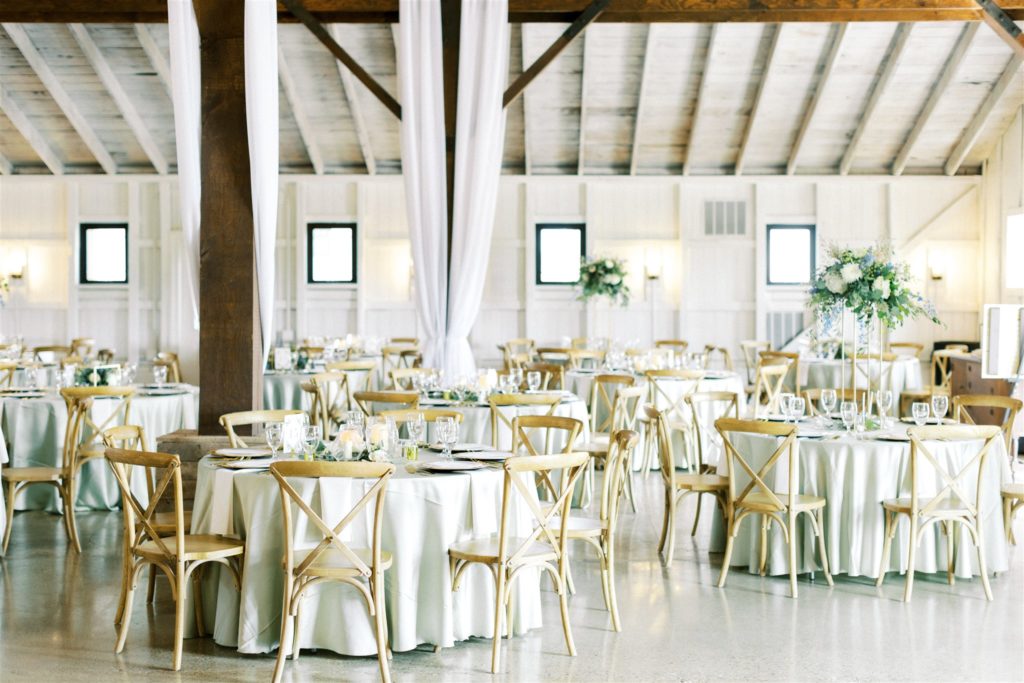 The wedding reception design had round table with wood crossback chairs and tall floral centerpieces inside the white willow farms wedding barn 