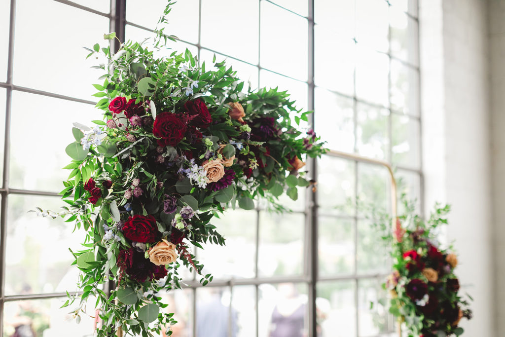 a close up shot of the greenery and red and peach roses that decorated the arch for the ceremony at the Clerestory 