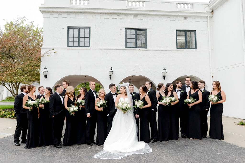 the bride and groom and their wedding party in classic black and white attire outside the woodstock country club