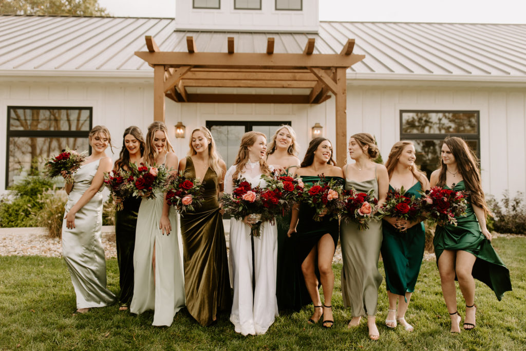 bridal party dressed in long dresses and holding large red bouquets in front of the front entrance to the wilds wedding venue