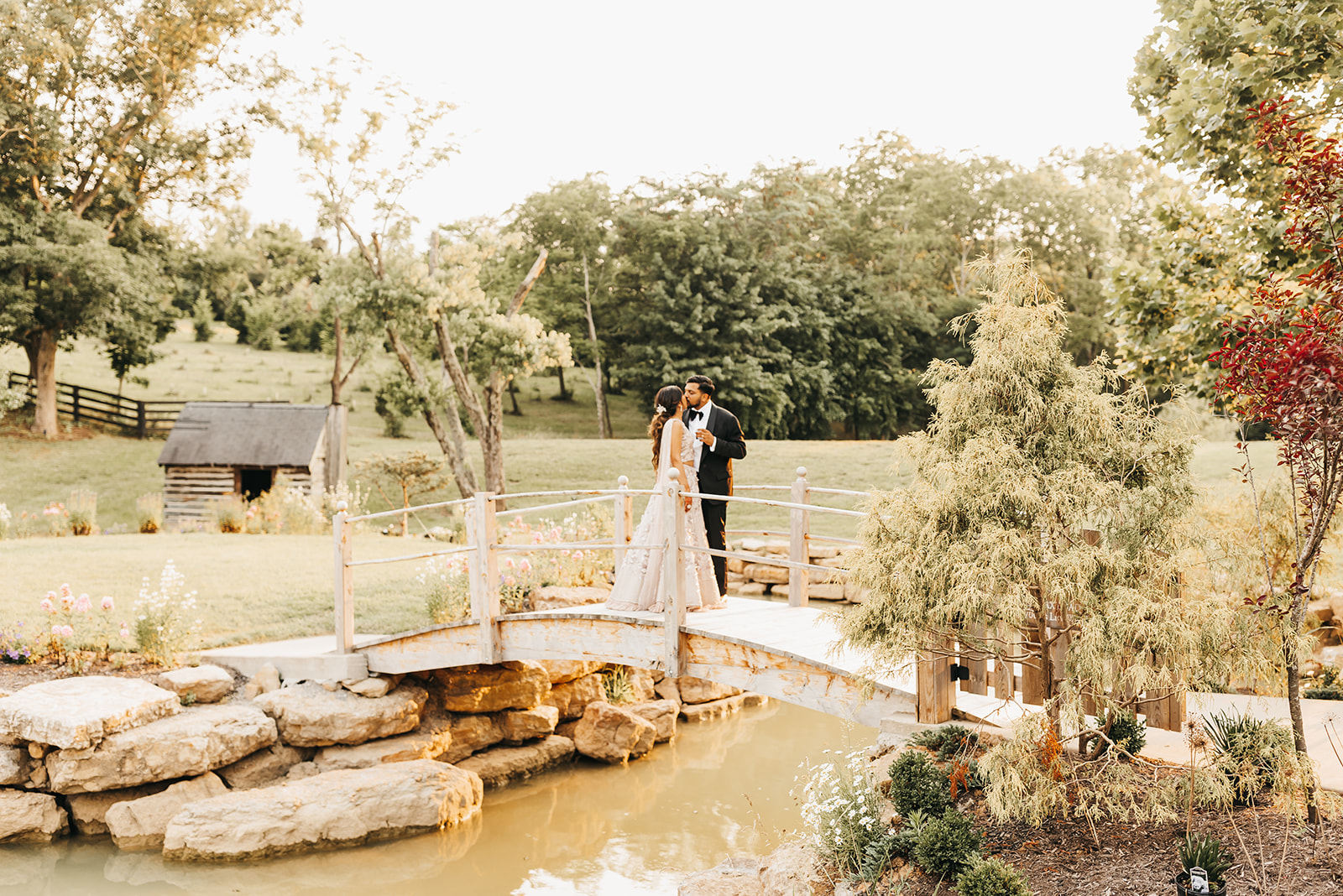 the bride and groom kiss on the small bridge going over the stream on the hazelnut farm property at sunset
