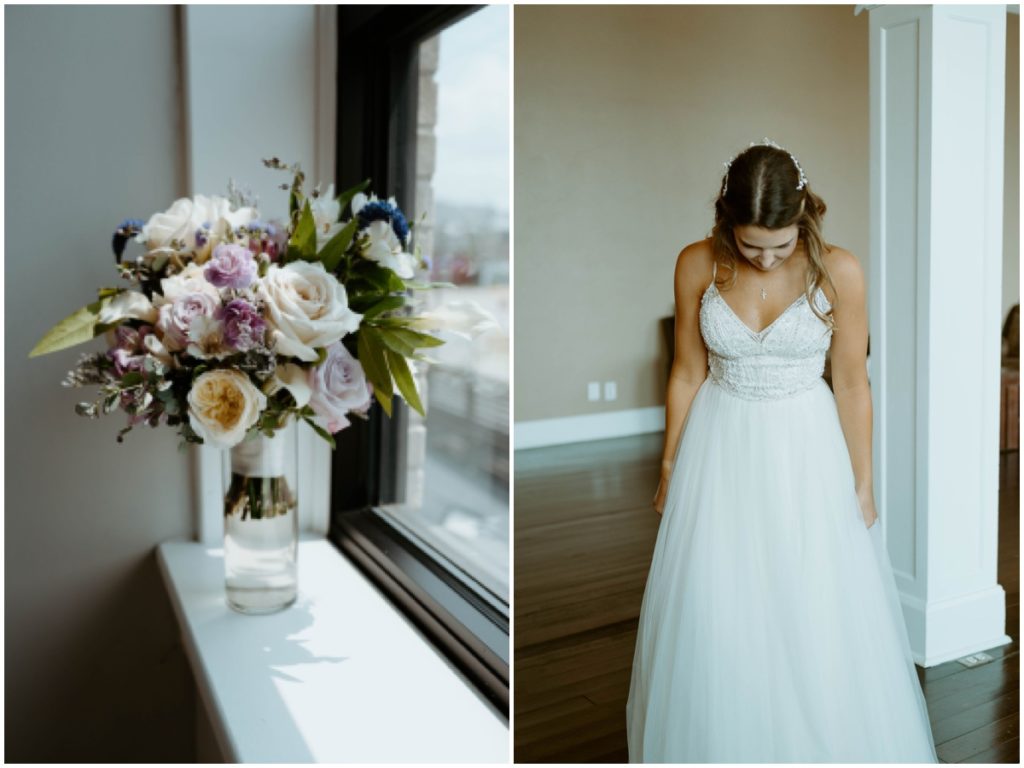 The bridal bouquet in a glass vase on a windowsill and the bride looking down at her wedding dress and she wears her wedding dress