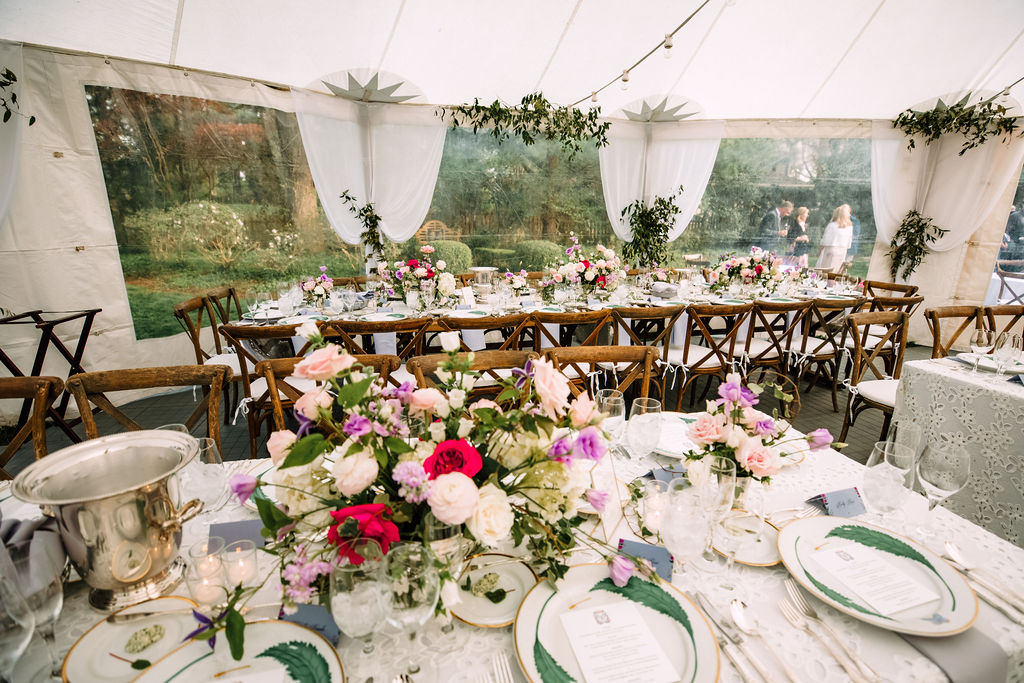 backyard wedding reception tent tables with white tablecloths, wood chairs, and white, pink, red and purple flowers