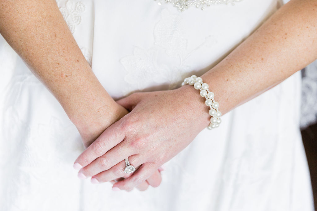 The brides diamond ring on her ring finger and a pearl bracelet. 