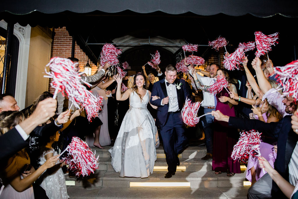The bride and groom are cheered by guests with red and white pom poms as they exit the Hurstbourne Country Club 