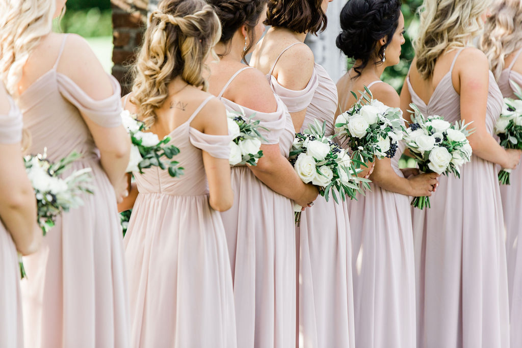 The bridesmaids at the ceremony, wearing pale pink dresses and holding white and green bouquets.