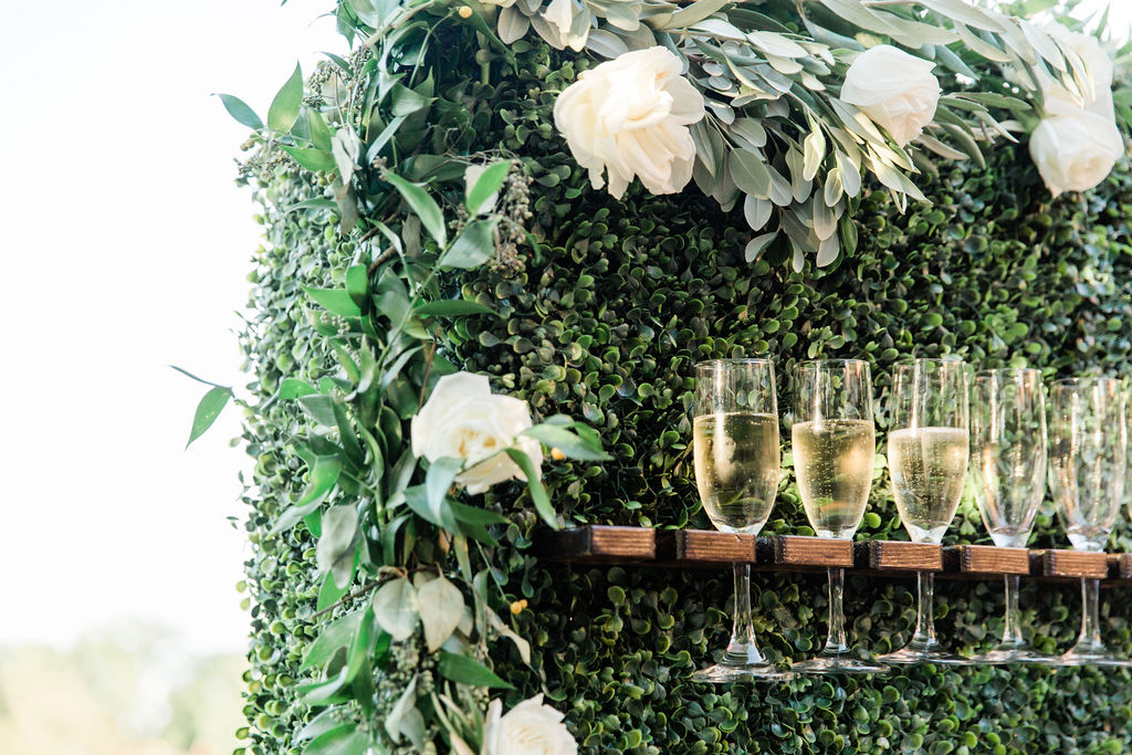 Close up of the champagne wall with greenery background and white floral trim