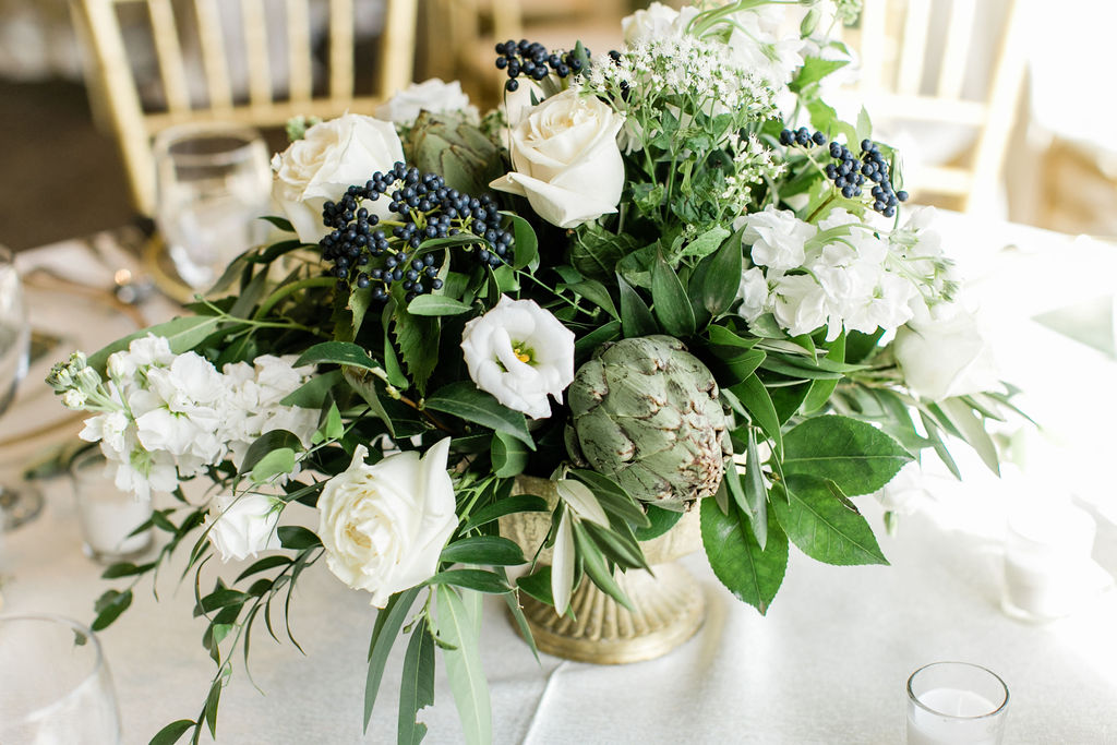 Reception table centerpieces consisting of white floral, mix of greens and navy with a gold vase 