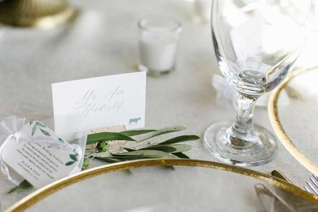 Close up of a white name card with blue ink, held by a wine cork and green embellishment