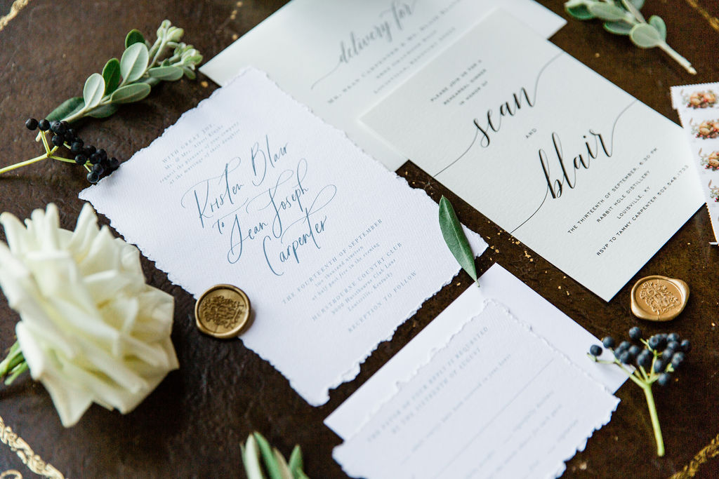 White stationary with blue and black ink, wax gold seals and floral accents around. 