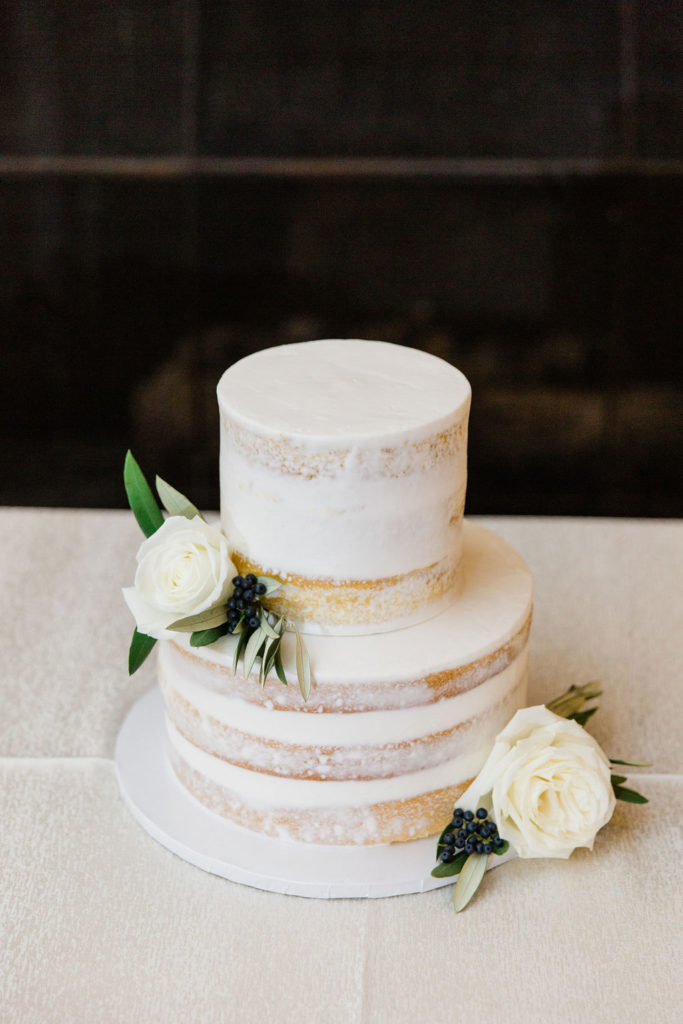 Simple, white, two-tiered cake with white roses, green leaves and navy berries