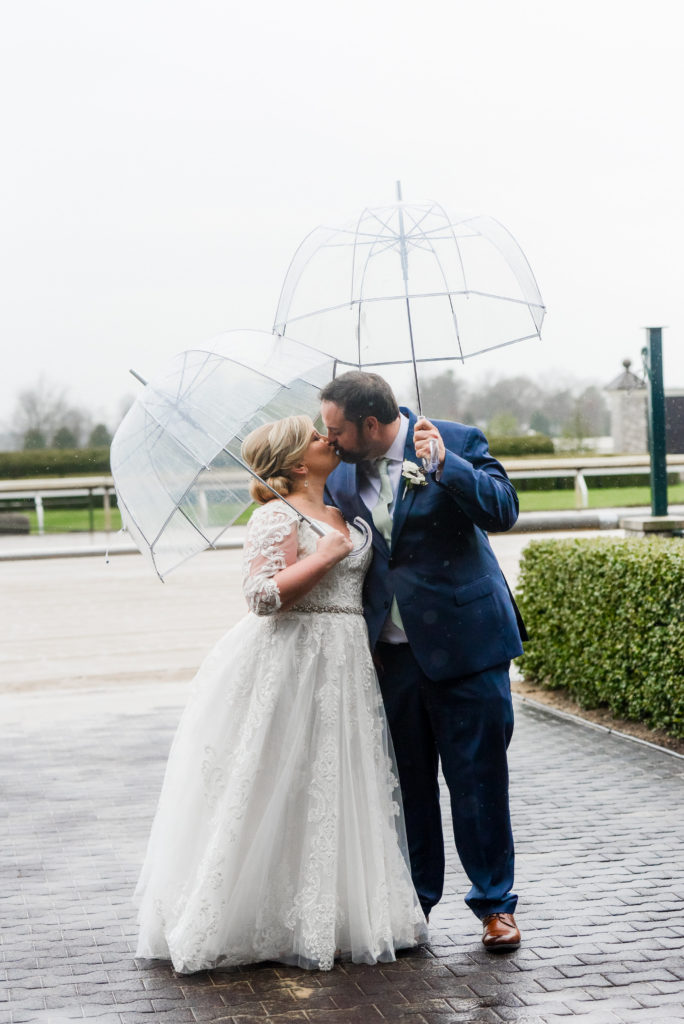 the bride and groom share a kiss underneath two umbrellas outside in the rain 