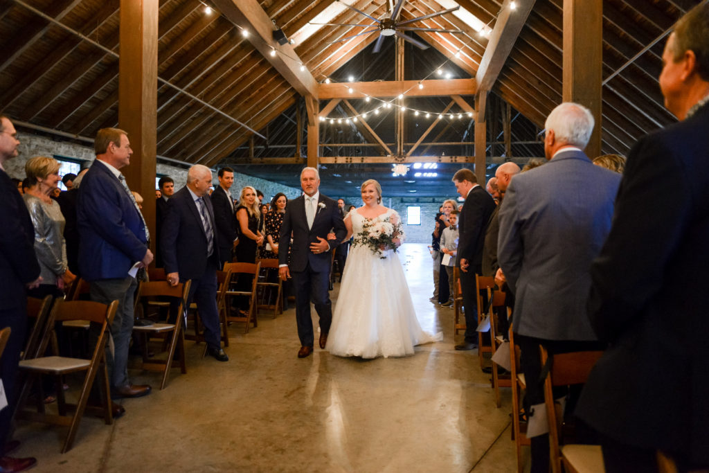 The bride is escorted down the aisle by her father inside the Keeneland Barn