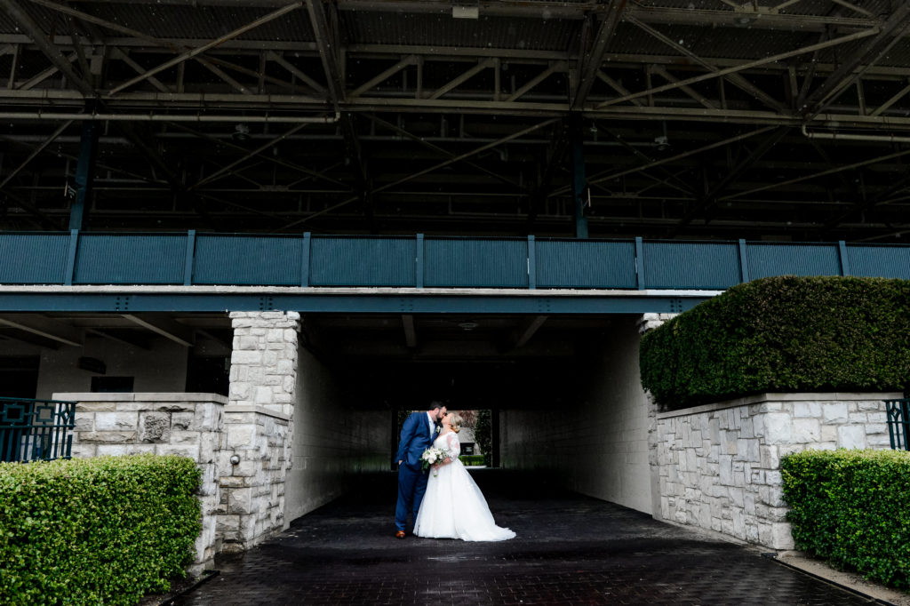 The bride and groom kiss outside of the Keeneland venue on a rainy day