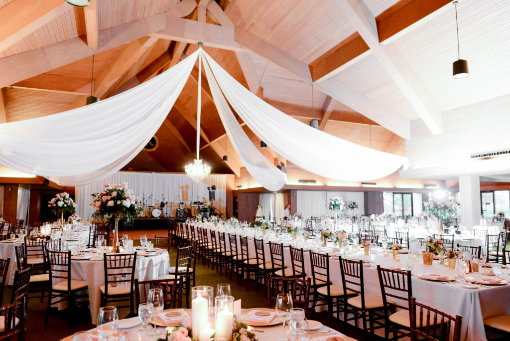 The reception space filled with tables, white linen, floral centerpieces, and white linen and chandeliers hanging from the ceiling