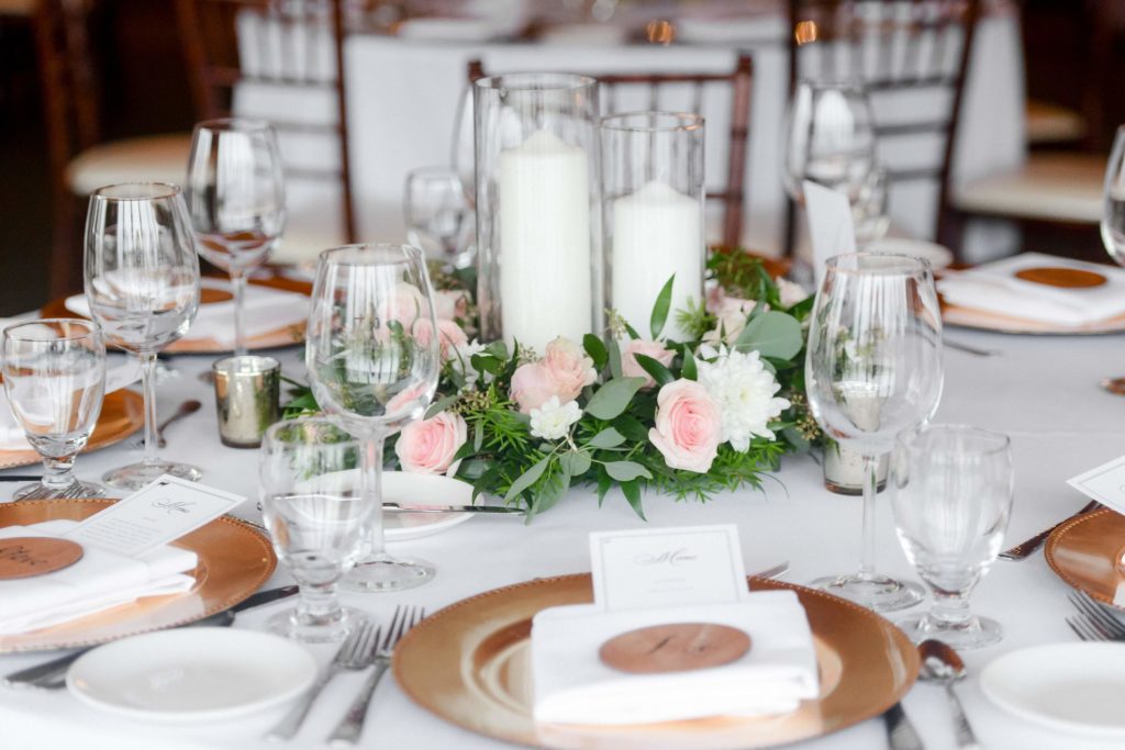This table had white candles with white and pink floral and greenery with gold chargers, glassware, and silver flatware