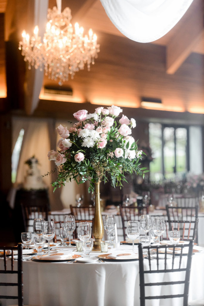 Tall floral centerpiece with white and pink flowers and greenery with a gold vase.