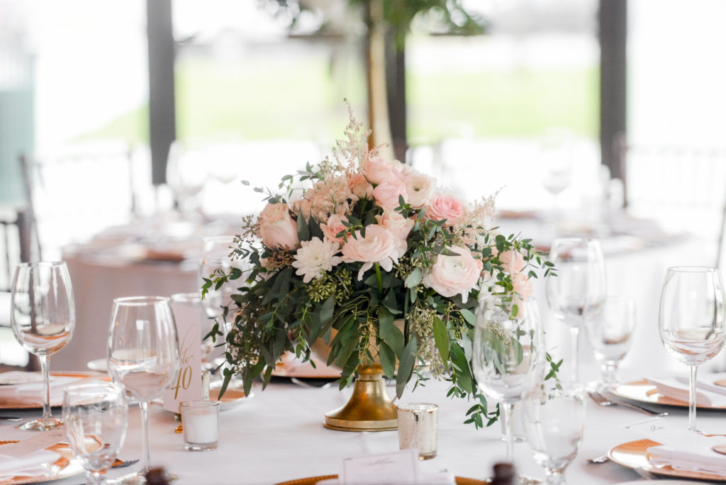 Pink and white flowers with greenery in a gold vase with small tea lights around centered on the table