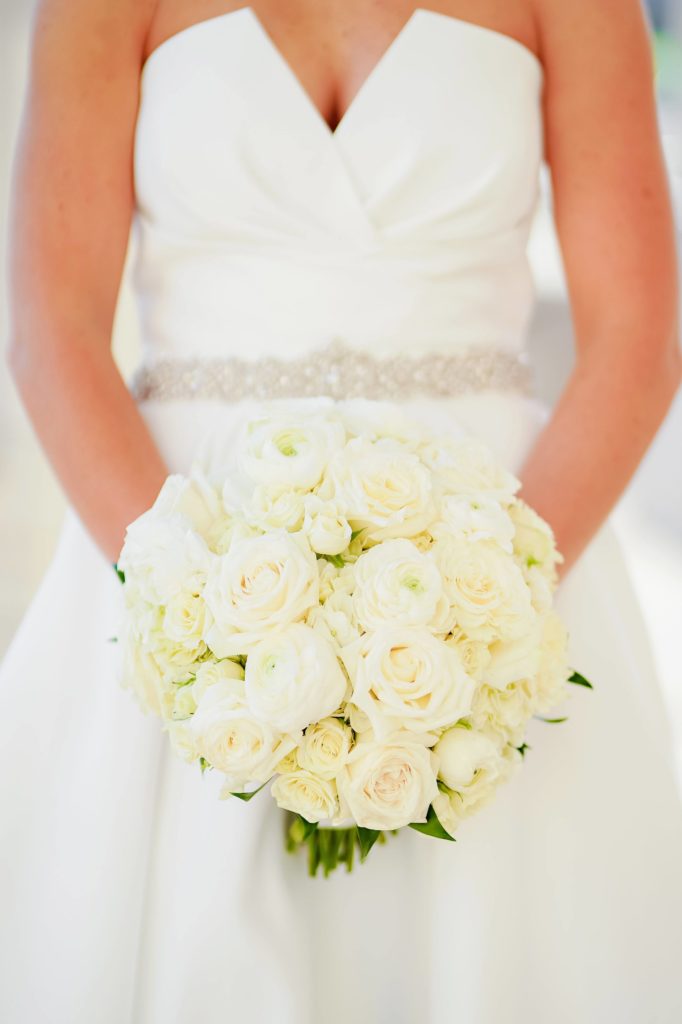 The bride in her white wedding dress holding her white floral bouquet in front of her