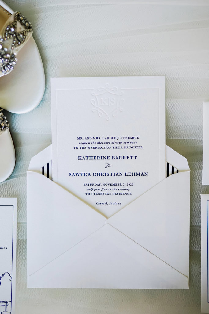 White and navy blue wedding invitations with bride and groom initial's pressed at the top