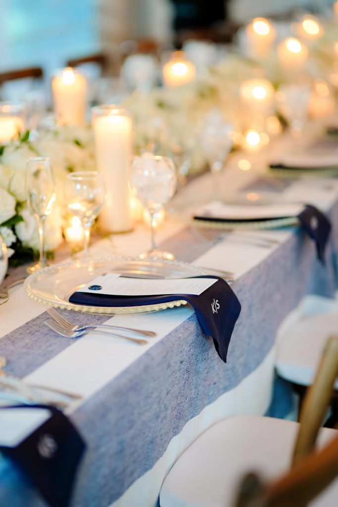 The reception table place setting with a place setting of china, a custom white menu card with navy writing, and a navy wax seal holding the guest’s place card.