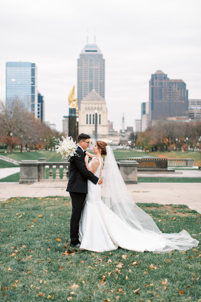 The bride and groom take a photo outside the Indianapolis central library with the Indianapolis skyline