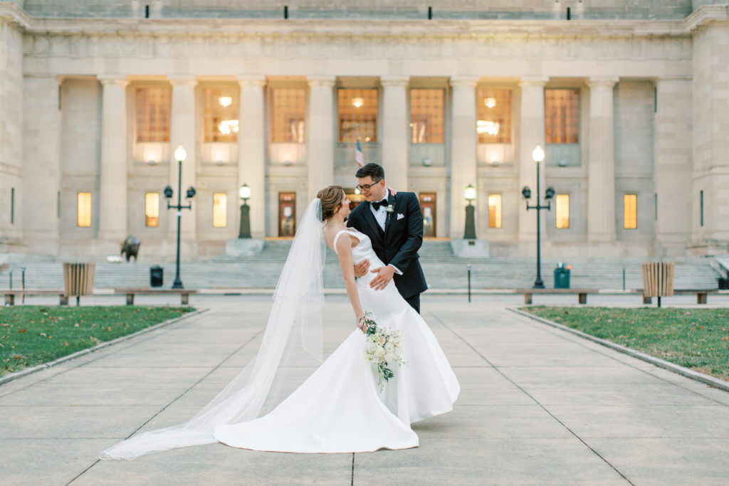 The bride and groom take a photo in front of the Indianapolis central library 