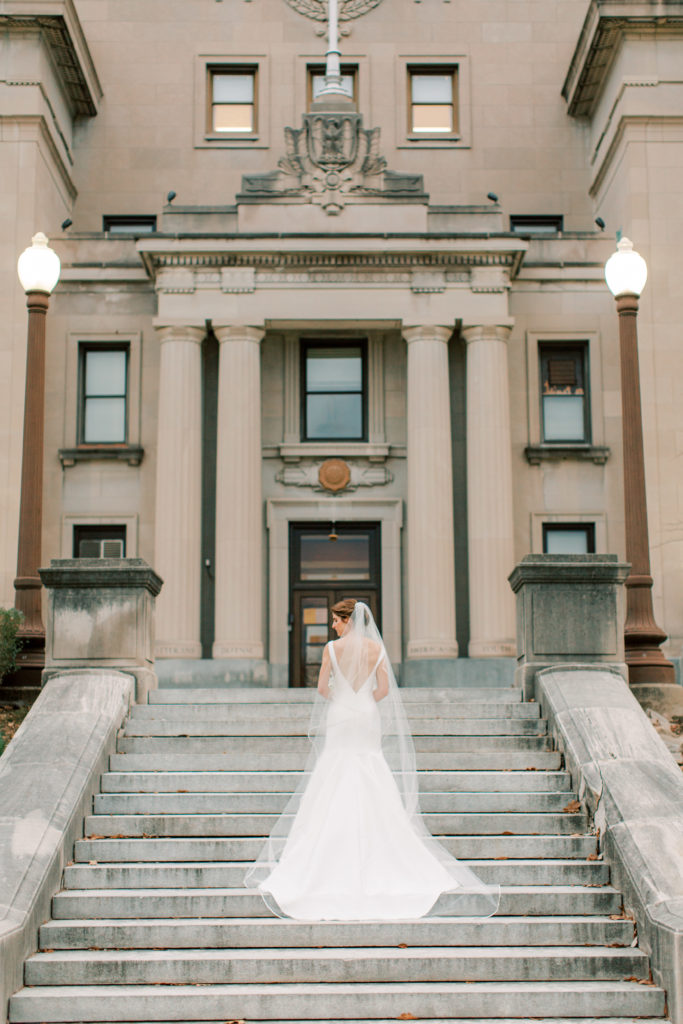 The bride takes a photo look away from the camera on the Indianapolis central library steps outside