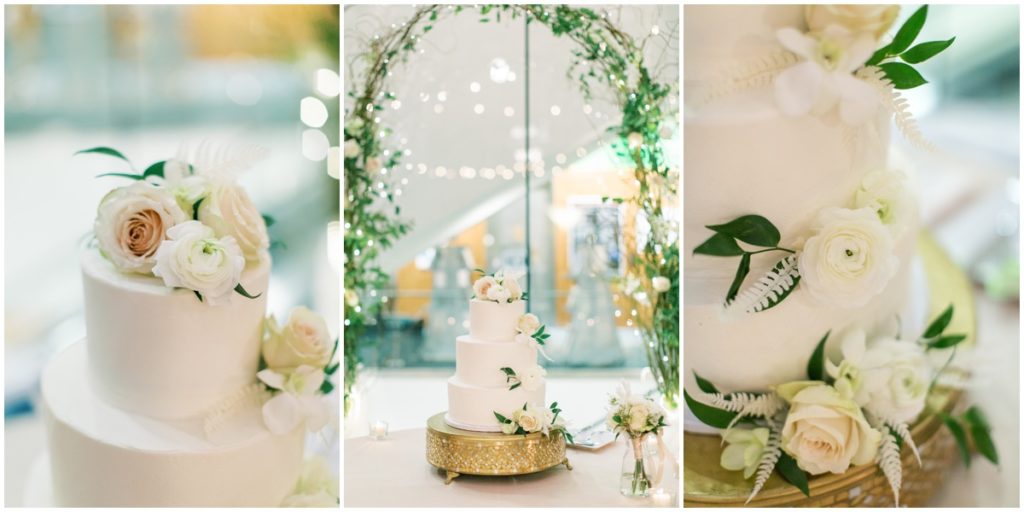 Three tiered white cake with floral accents underneath an archway of greenery