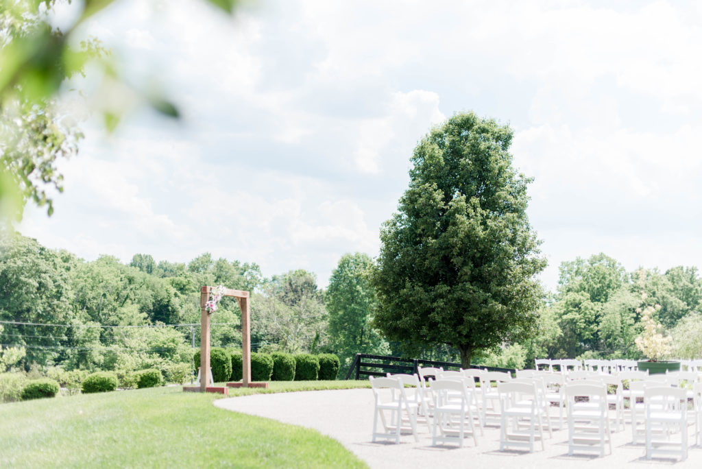 an intimate wedding ceremony set up on private property in Kentucky consisted on a wooden arch with floral accents, and white chairs