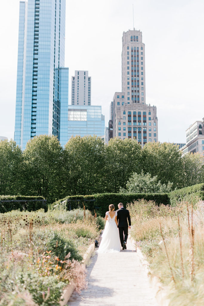 The bride and groom walk in a park near the city winery with skyscrapers of chicago in the background