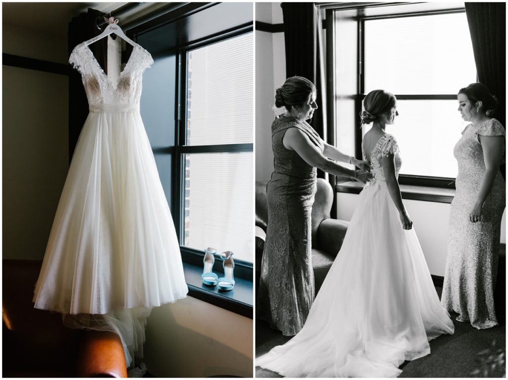 The bride's wedding dress is hung next to a hotel window and the bride is helped into her dress by two of her bridesmaids