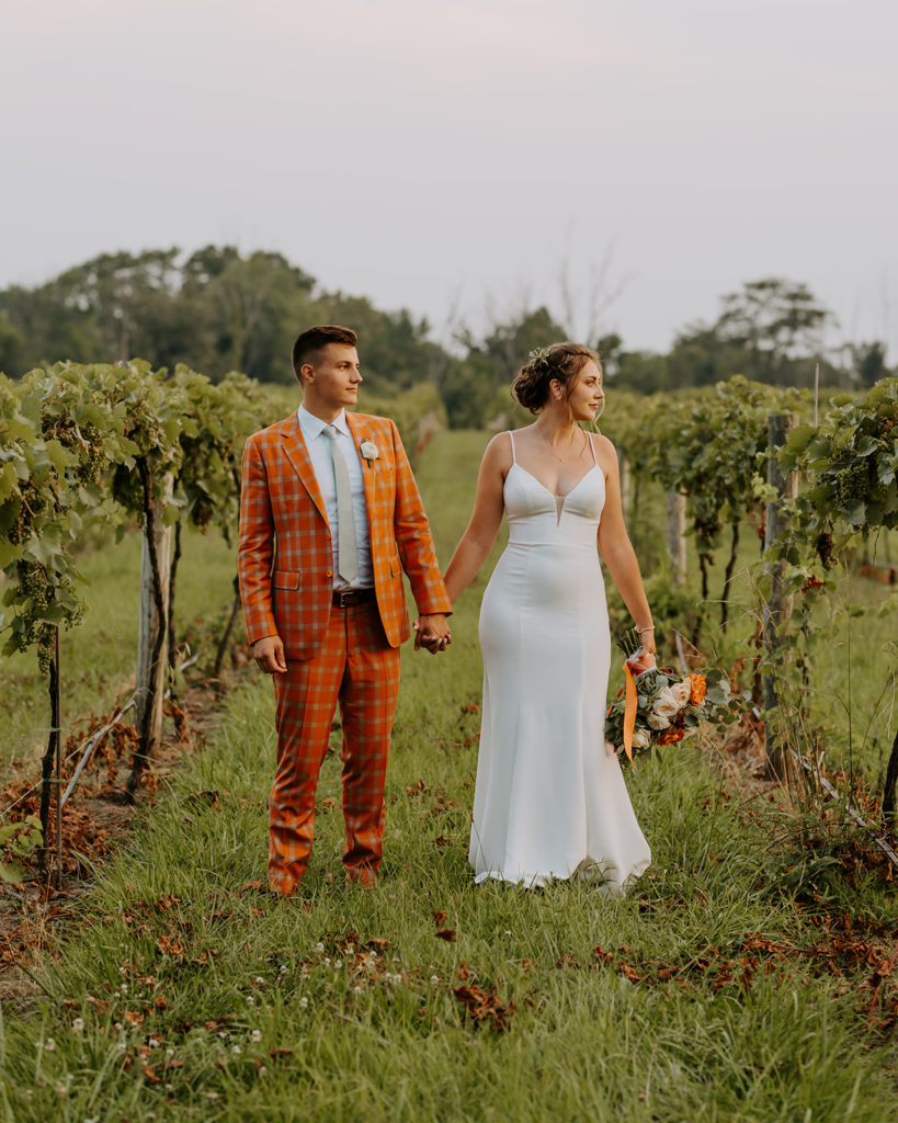 The bride and groom walk through the vineyards at daniel's vineyard at their winery wedding