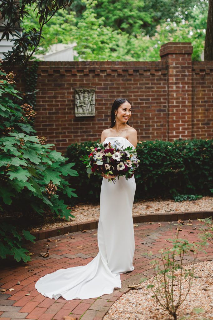 The bride has a solo photo with her in her long white wedding dress with her bouquet of flowers in an outdoor courtyard