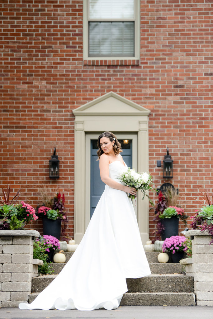 The bride poses with her dress and bouquet outside of her parent's classic brick house in indianapolis