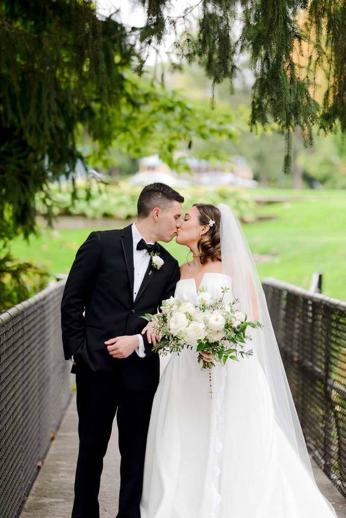 the bride and groom share a kiss on an outdoor bridge on the grounds of the woodstock country club
