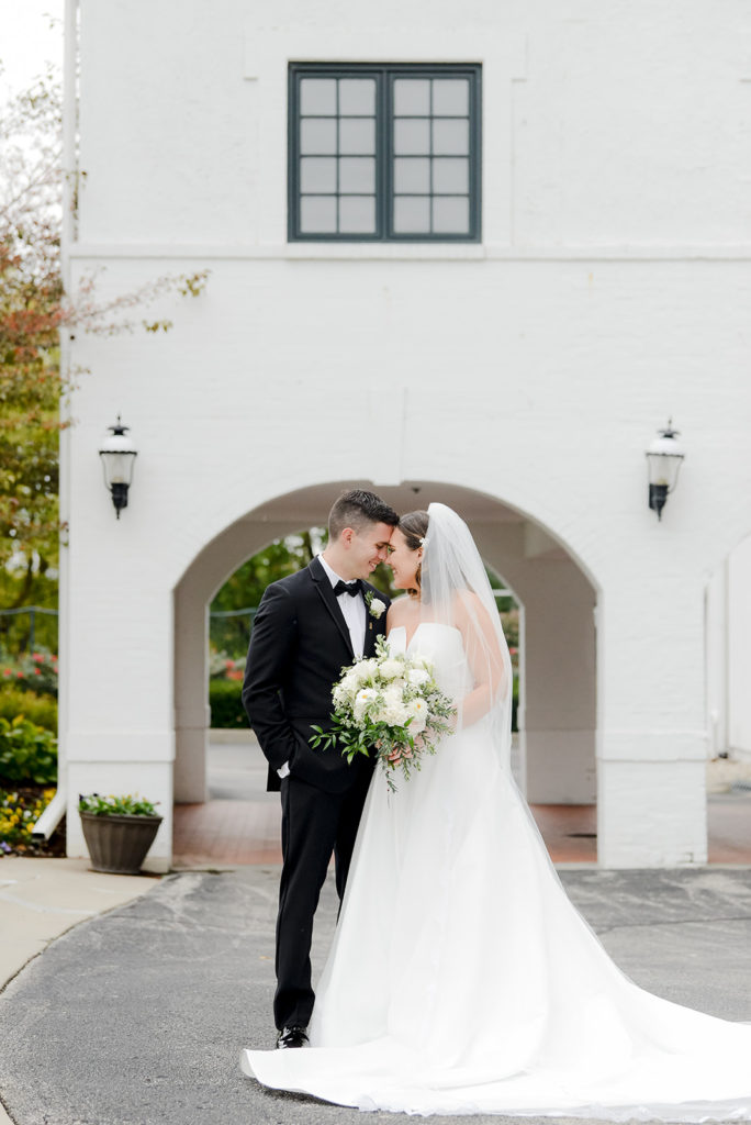 the bride and groom take a sweet photo in front of the archways in the driveway of the woodstock country club in indianapolis