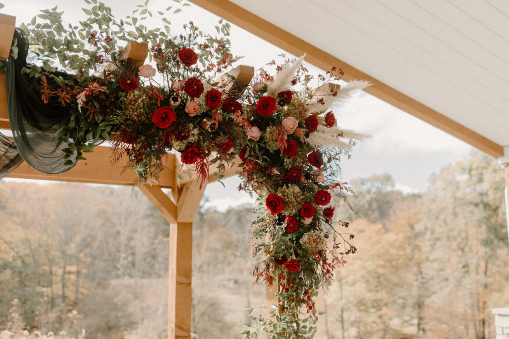 close up shot of the red flowers and greenery accent on the pergola arch