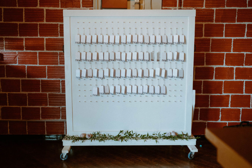 a white seating chart on wheels in front of a brick wall inside the biltwell event center
