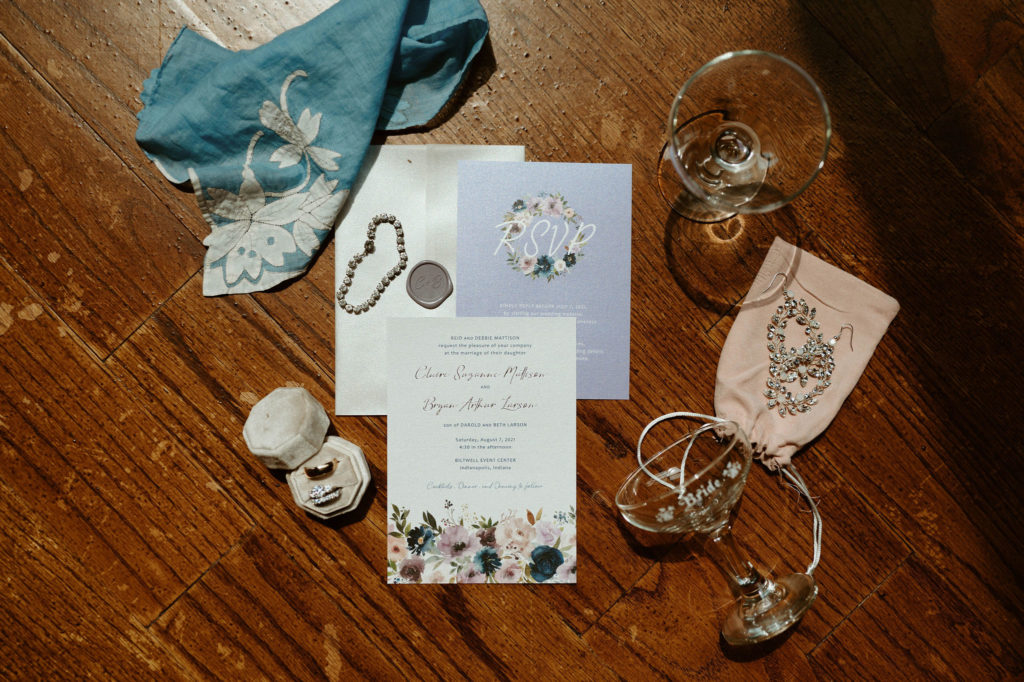 wedding invitations with jewelry, champagne glasses and blue fabric on a wooden table. 