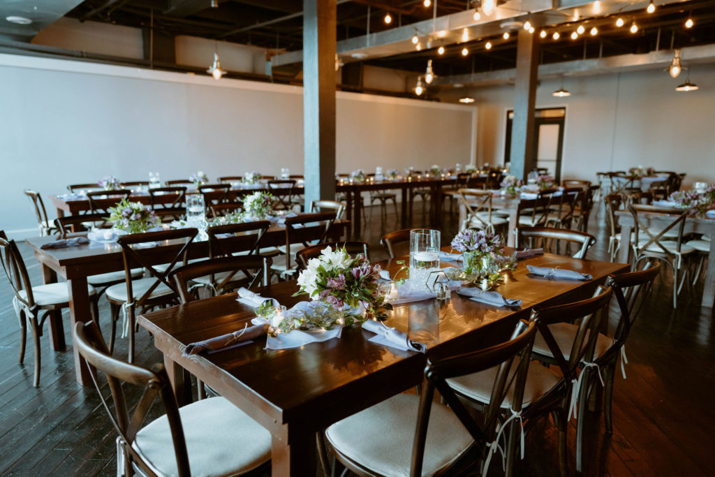 the biltwell event center with long wooden tables and chairs with lavender linens, lavender flowers and tealight candels