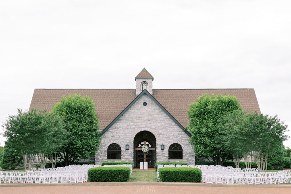 Outdoor ceremony location with white chairs, green trees and wooden cross at Keeneland wedding venue