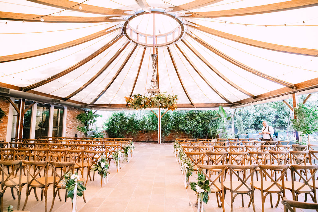 The Apiary wedding ceremony site in their outdoor garden with white canopy, wooden chairs and fresh greenery