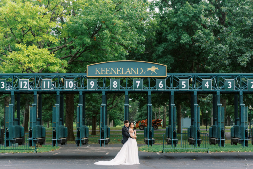 Bride and groom embrace in front of Keeneland racing gate on the grounds of the Keeneland Wedding Venue