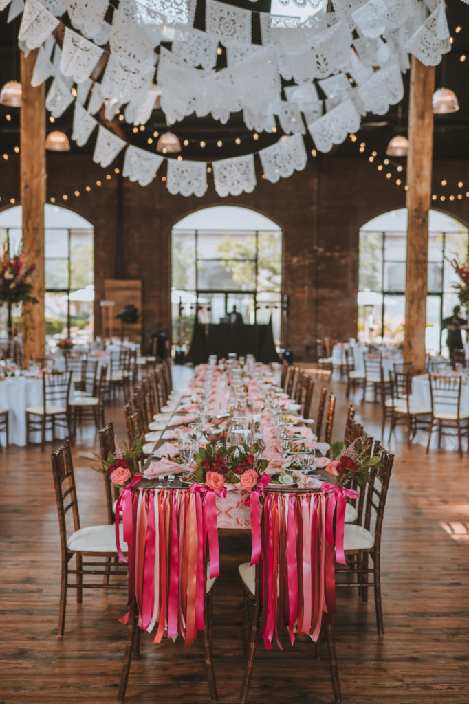 Festive wedding reception decorations with pink and orange flowers, ribbon, lights and linen at The refinery in Louisville KY 