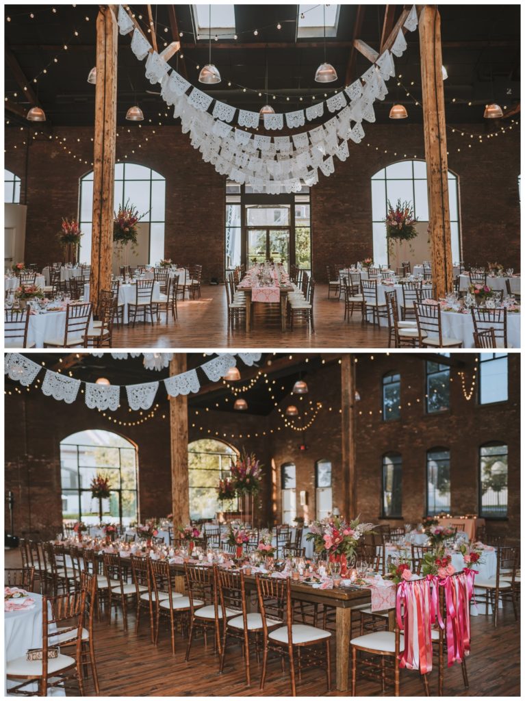 Festive wedding reception decorations with pink and orange flowers as centerpieces, white flags and market lights hanging from the rafters, and pink ribbon highlighting the bride and groom's seats at The refinery in Louisville KY 