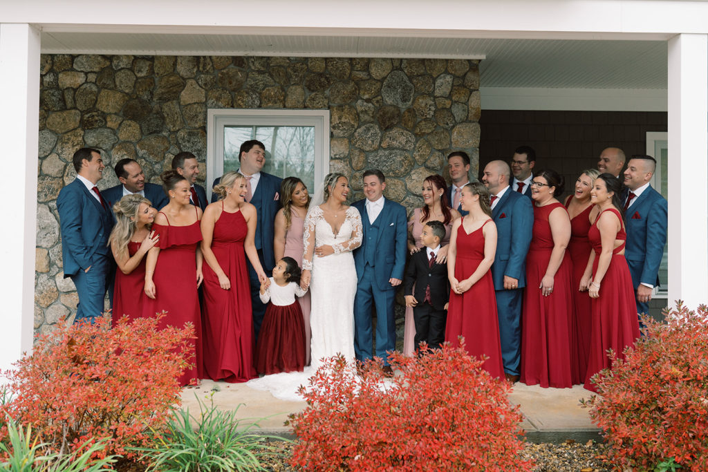 The groomsmen in navy blue suits and the bridesmaids in long red dresses surround the bride and groom on the patio of labelle winery